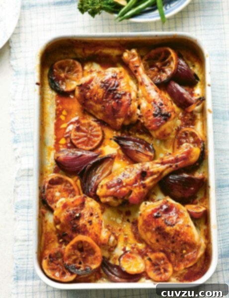 A metal sheet pan filled with lemon ginger chicken legs and thighs with shallots and lemon slices.