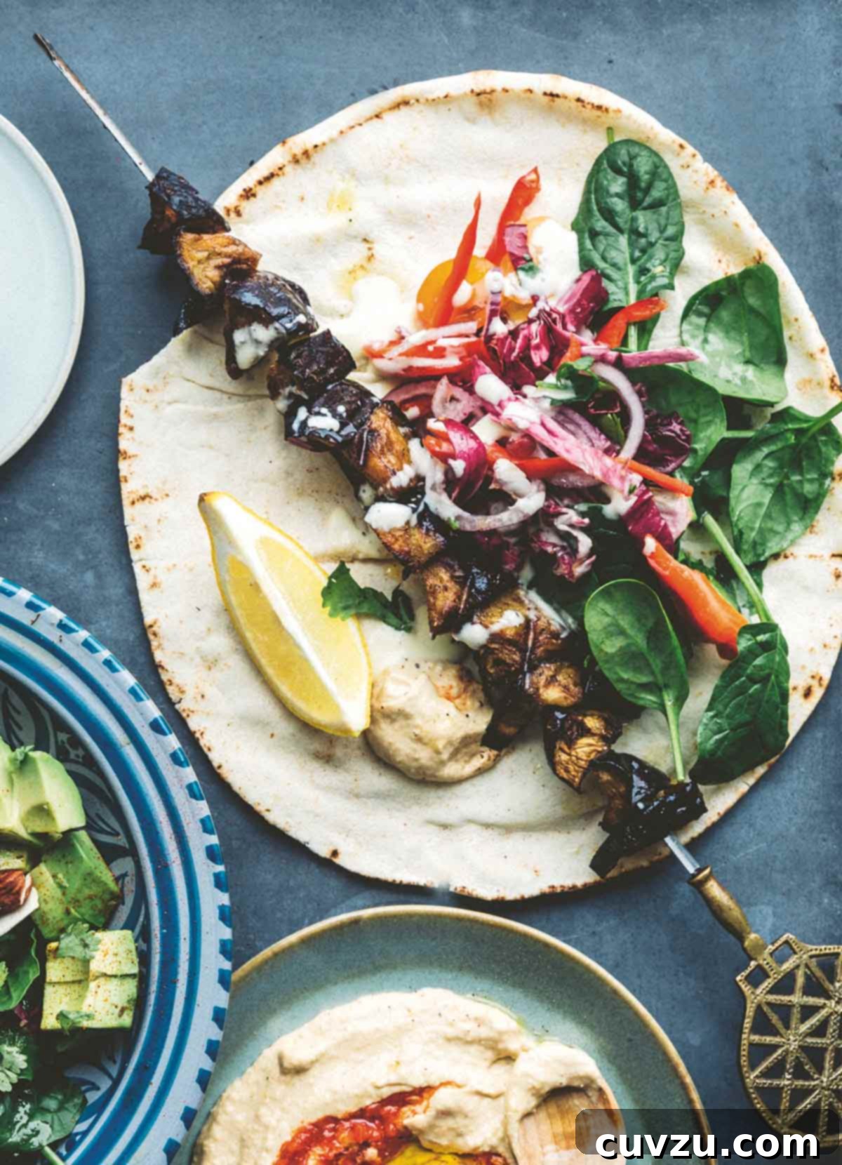 An eggplant kebab on a tortilla with fresh spinach, garlic sauce, and cabbage.