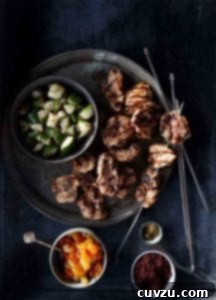 A metal plate with chunks of cooked turkey, a turkey kebab, and a dish of cucumber salad.