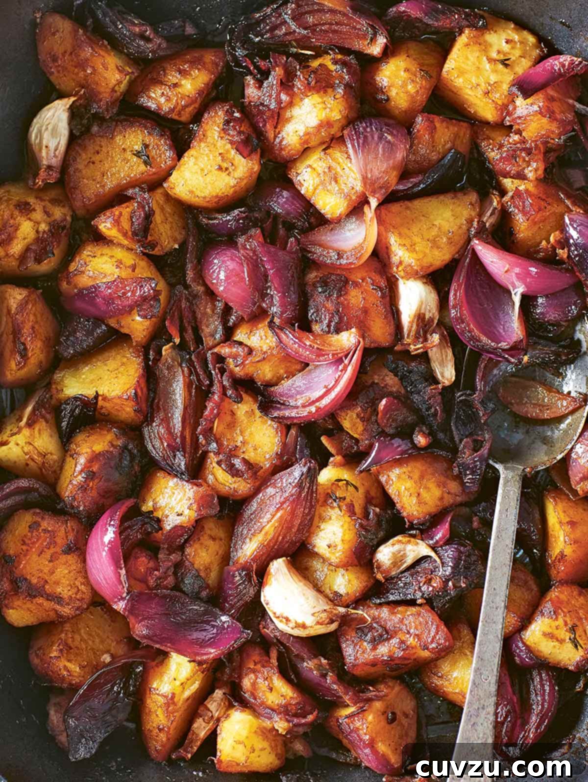 Sweet and Tangy Balsamic Roasted Potatoes 2 Close-up of golden-brown balsamic roasted potatoes with caramelized red onions and garlic in a roasting pan, garnished with fresh thyme.