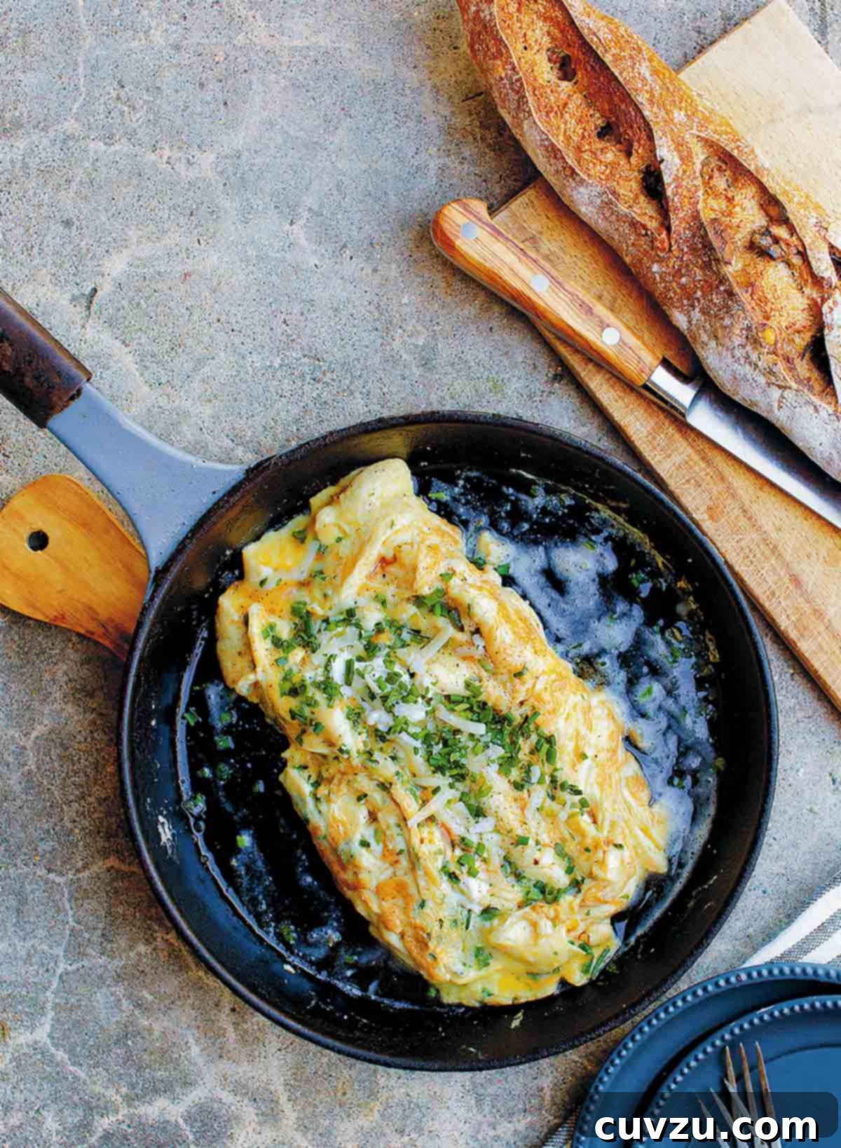 A black skillet containing a cheese omelet, topped with chives and Gruyere.