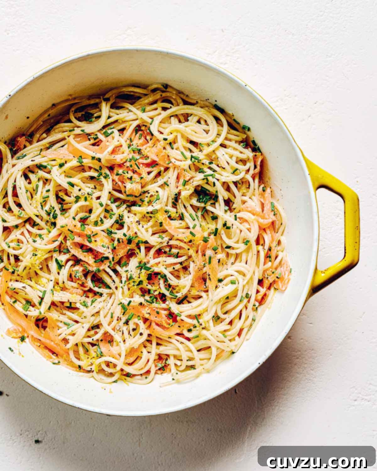 A yellow and white pot filled with smoked salmon pasta and garnished with fresh chives.
