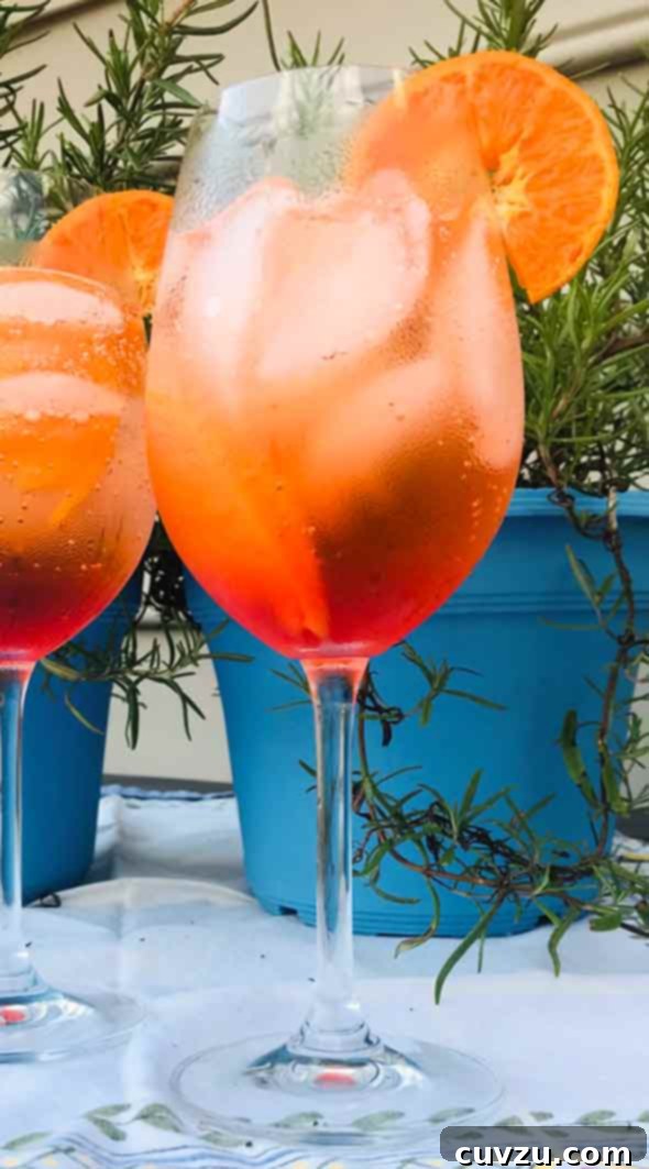 Two wine glasses on a patio table, filled with a bubbly orange cocktail, ice and orange slices.