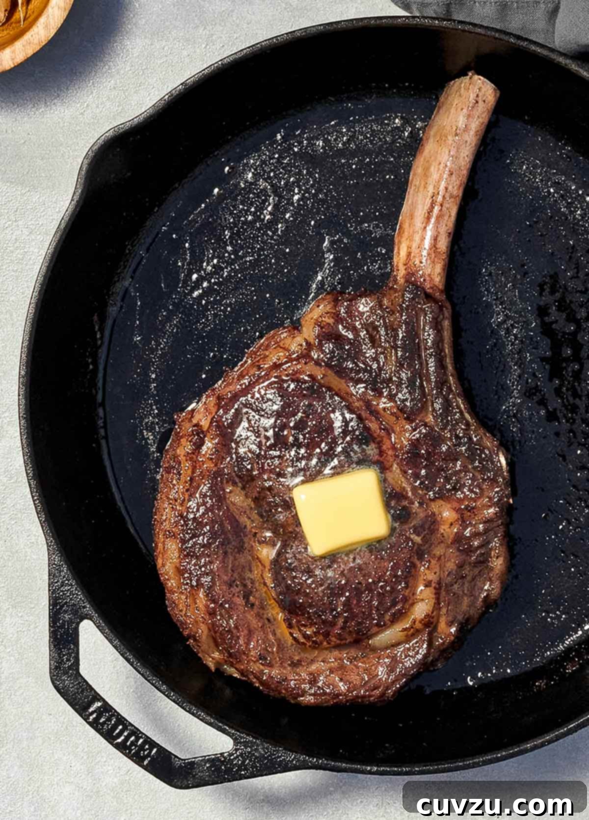 Cinnamon-Kissed Rib-Eye Perfection 2 A large rib eye steak with a pat of butter on top, in a cast iron pan, ready for basting.