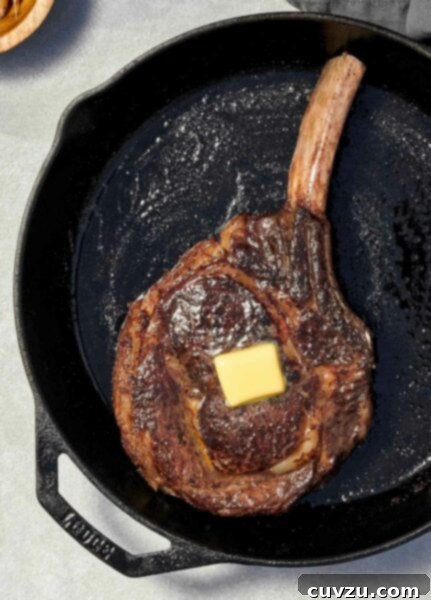 A large rib eye steak with a pat of butter on top, in a cast iron pan.