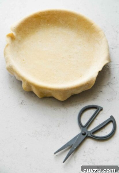 Empty pie crust in a pie plate, with kitchen shears next to it.