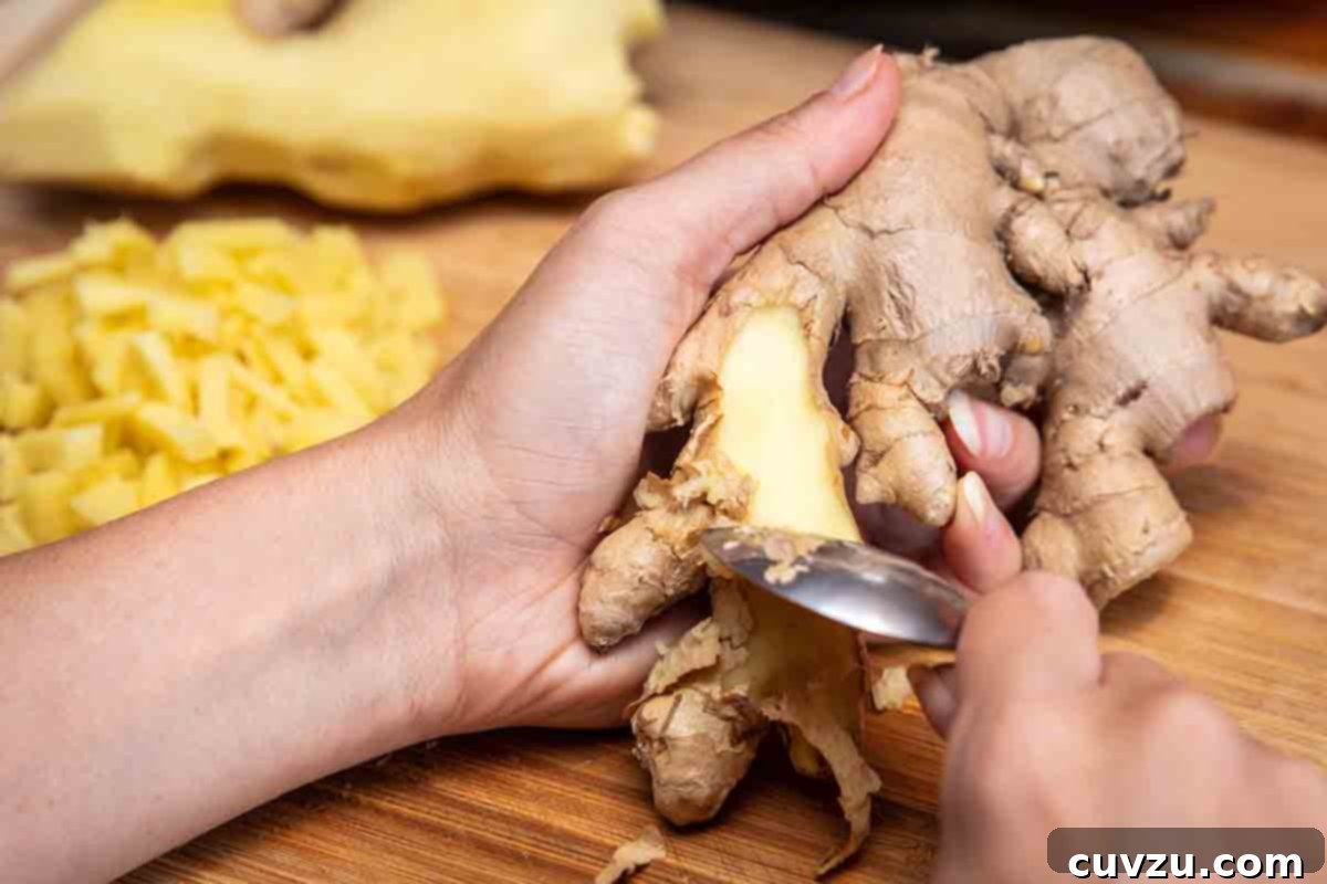 A woman's hand holding a ginger root while peeling it with a spoon.