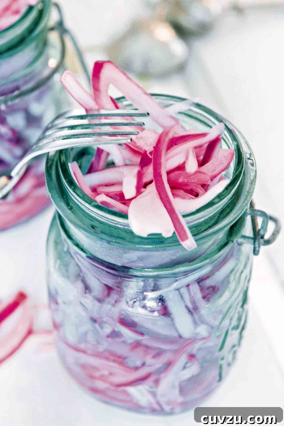 A canning jar overflowing with pickled red onions and a fork resting on the jar.