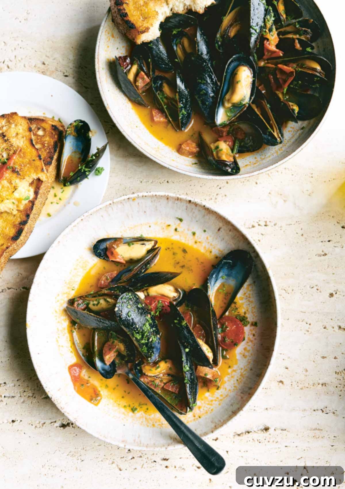 Two pristine white plates showcasing beautifully steamed mussels. The mussels are nestled in a vibrant, savory sauce featuring blistered cherry tomatoes, robust slices of Spanish chorizo, and a generous sprinkle of fresh green parsley. A side of perfectly toasted, buttery bread awaits to absorb the rich broth.