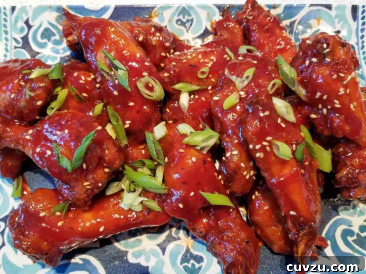 Sweet and spicy chicken wings, garnished with green onions and sesame seeds on a blue and white plate.