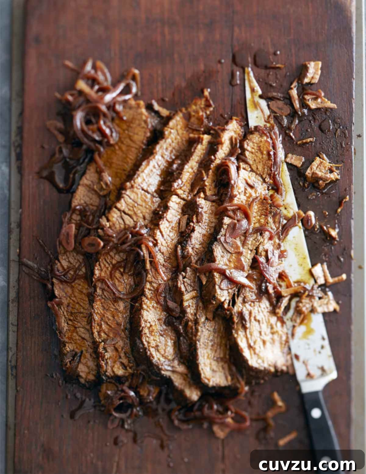 Rosh Hashanah Feasts: 11 Must-Try Recipes 3 A sliced piece of braised brisket with red wine and honey laying on a cutting board with a large knife and covered with braised onions.