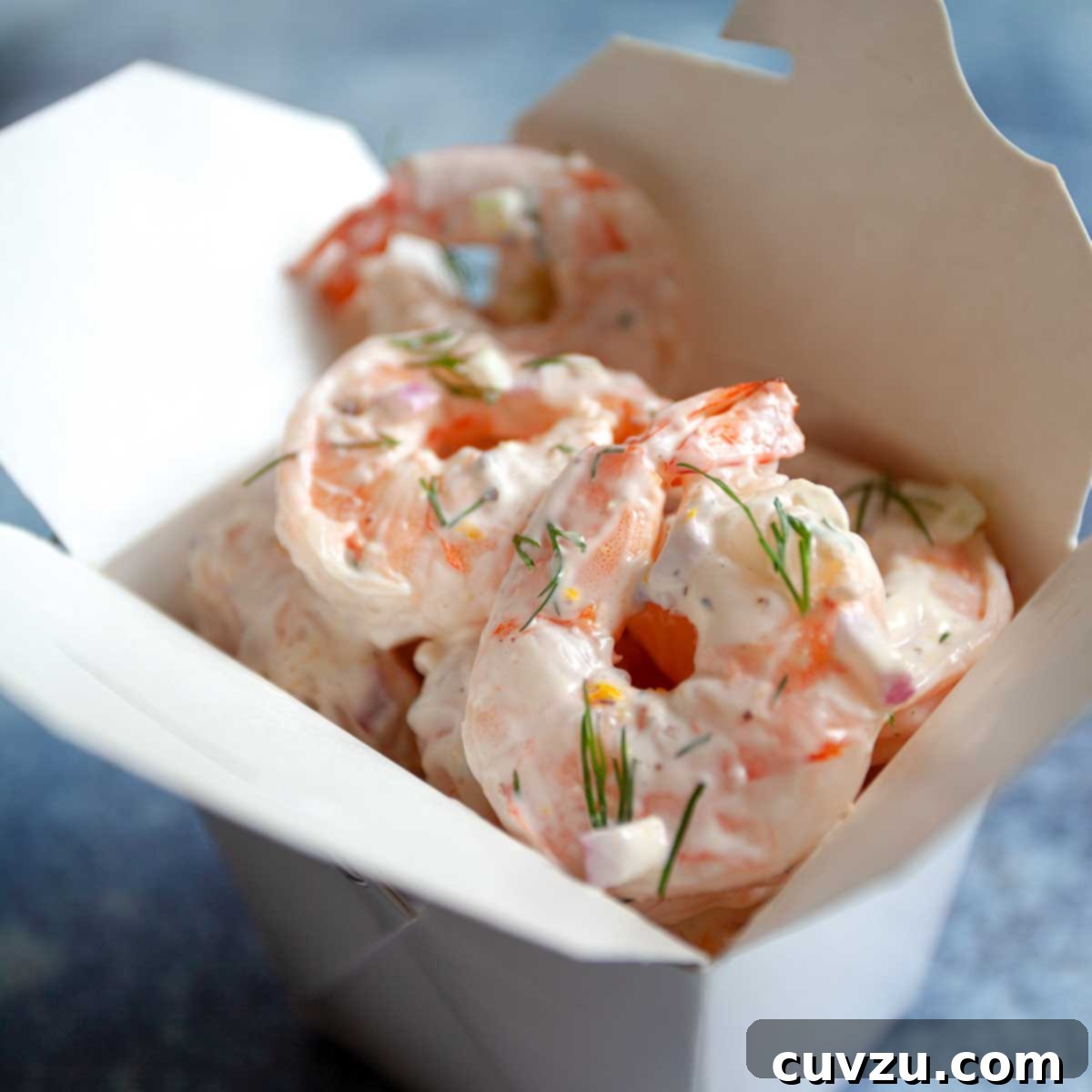 Shrimp salad garnished with fresh dill in a cardboard takeout container, a perfect elegant dish for any gathering.