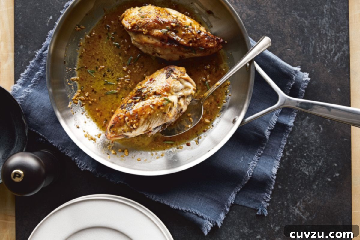 A cast-iron skillet featuring Chrissy Teigen’s perfectly crispy-skinned chicken, glistening with a vibrant lemon-rosemary pan sauce.