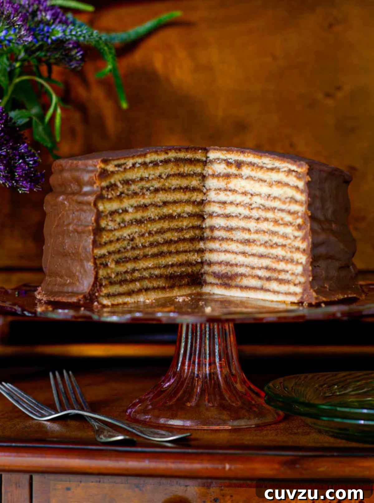 Trisha Yearwood's decadent chocolate torte on an elegant cake stand, with a section cut from it to display its impressive 12 layers of vanilla cake and rich chocolate glaze.