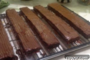 Slathering the melted chocolate evenly over the Rainbow Cookie cake layers.