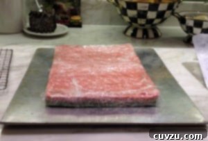 Red rainbow cookie caked baked and resting on silver baking sheet wrapped in plastic wrap.