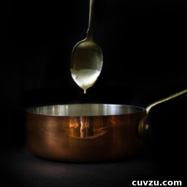 A spoonful of mustard cream sauce dripping in a copper pot