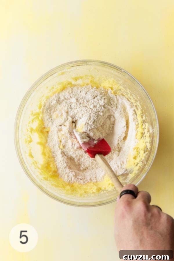 Zesty Lemon Loaf 11 A hand folding flour mixture into wet ingredients using a red silicone spatula.