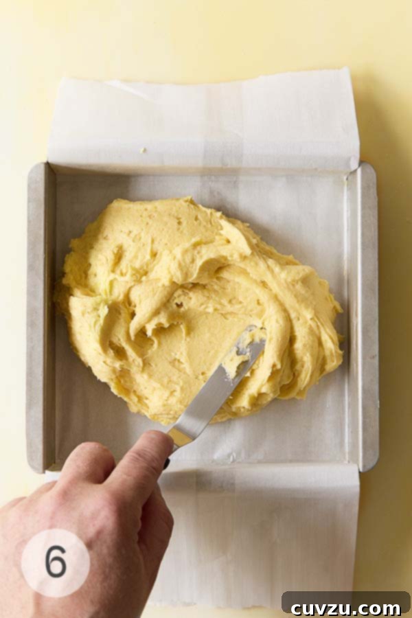Zesty Lemon Loaf 12 Cake batter being spread evenly into a parchment-lined square cake pan.