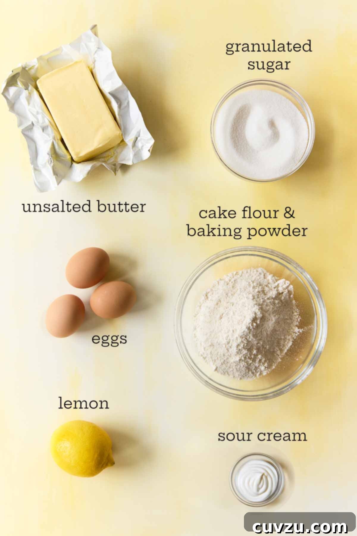 Zesty Lemon Loaf 6 Overhead view of lemon drizzle cake ingredients, including eggs, butter, sugar, lemon, sour cream, and flour with baking powder.