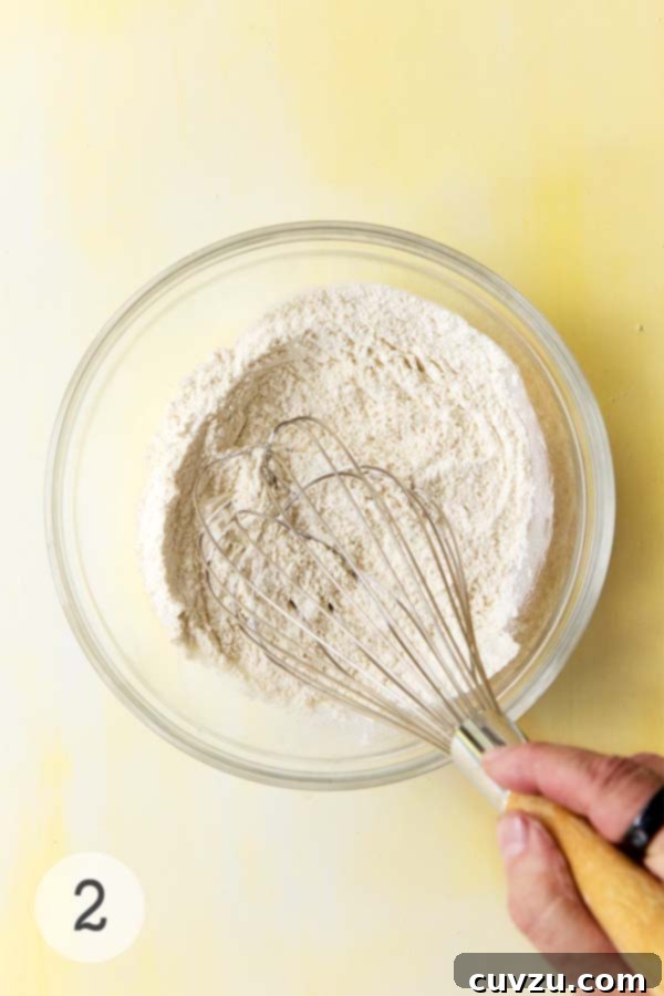 Zesty Lemon Loaf 8 Dry ingredients for lemon drizzle cake being whisked in a clear glass bowl with a wooden-handled whisk.