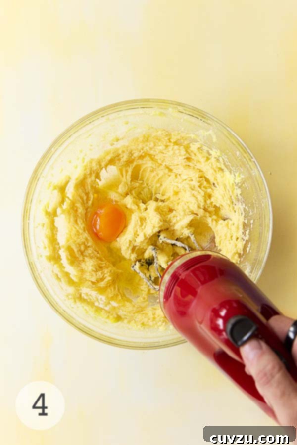 Zesty Lemon Loaf 10 Beaten butter and sugar with egg being mixed using a red handheld electric mixer.