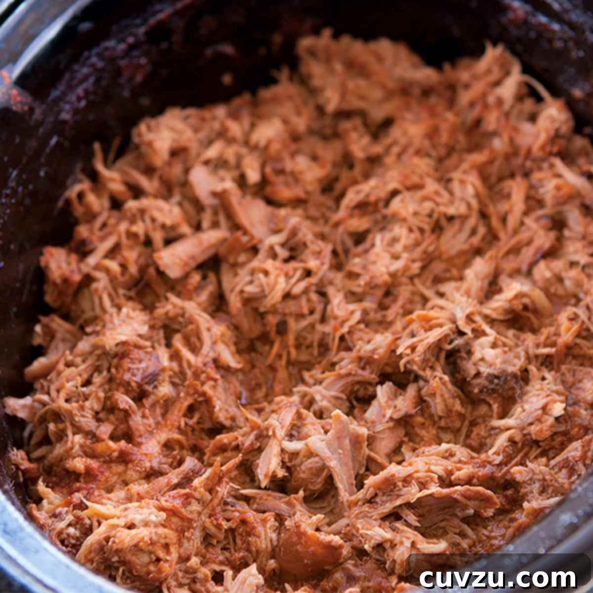 A slow cooker insert filled with shredded slow cooker pulled pork, ready to be served.