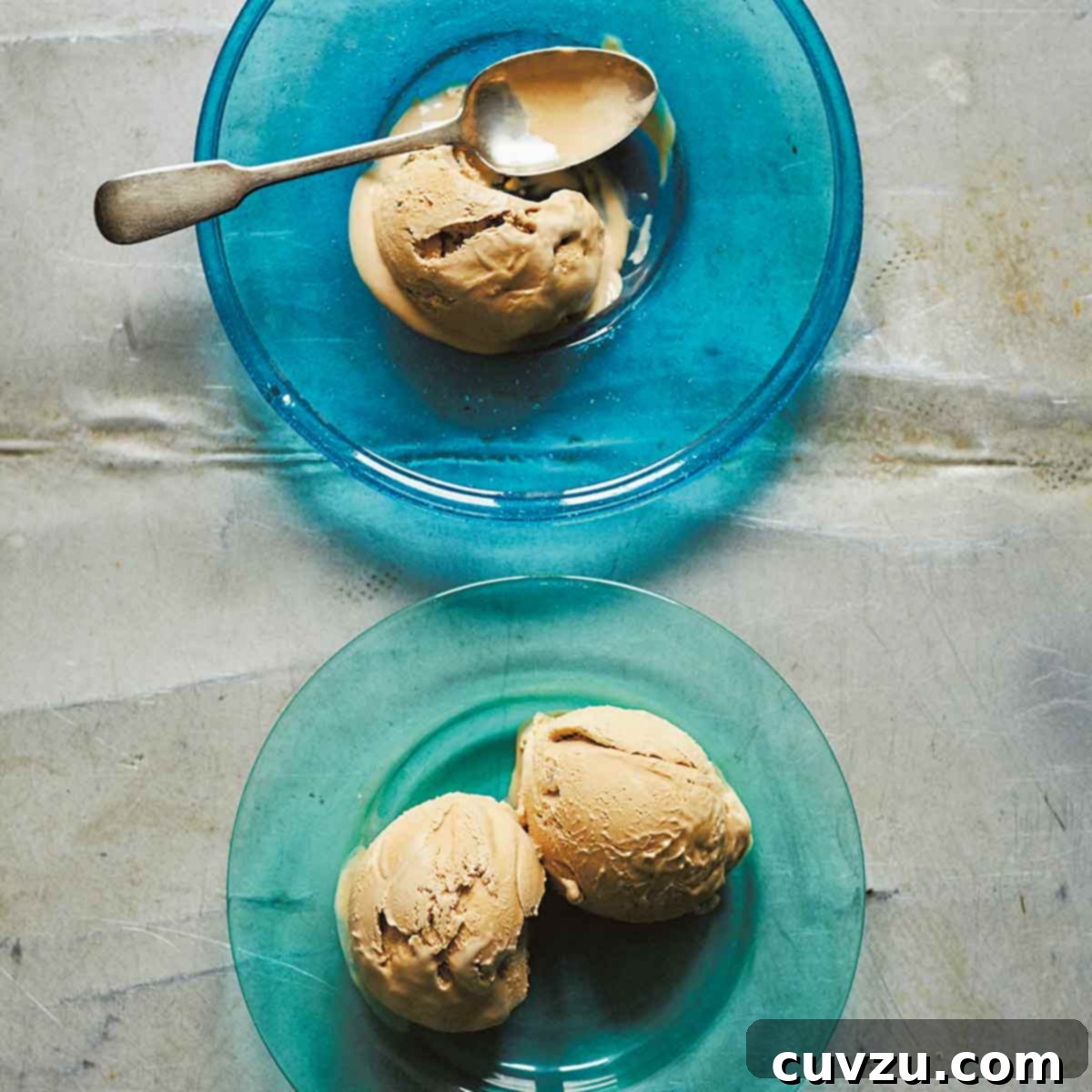 Two scoops of rich Turkish coffee ice cream served in elegant blue glass plates, accompanied by a spoon.
