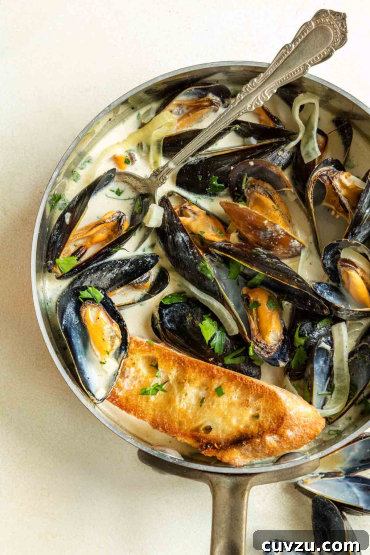 Decadent Mussels with Garlic Wine Cream 7 A lustrous copper saucepan brimming with an exquisite presentation of mussels nestled in a creamy white wine garlic sauce, elegantly garnished with fresh lemon wedges.