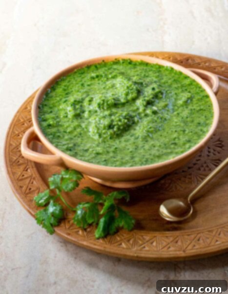 Schug in a pottery bowl, on a wooden plate with a spoon and garnished with cilantro.