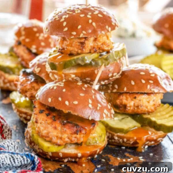 Nashville Heatwave Sliders 4 Nashville hot chicken sliders, piled up on a plate with sesame seeds and hot sauce.