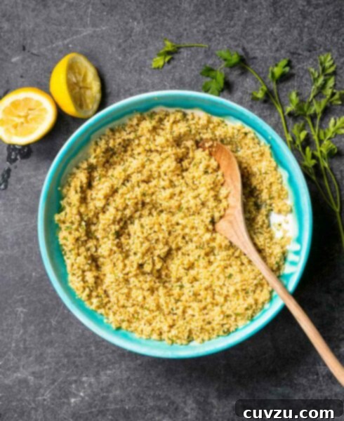 Baked quinoa with lemon and parsley in a turquoise bowl with a wooden spoon, surrounded by lemon halves and parsley sprigs.
