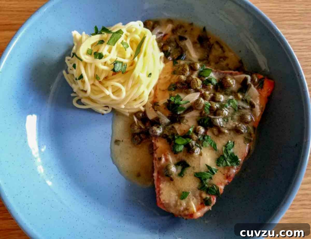 Zesty Lemon Salmon Piccata 5 A perfectly portioned lemon salmon piccata fillet on a vibrant blue plate, elegantly served alongside a swirl of spaghetti noodles, showcasing a delicious weeknight meal.