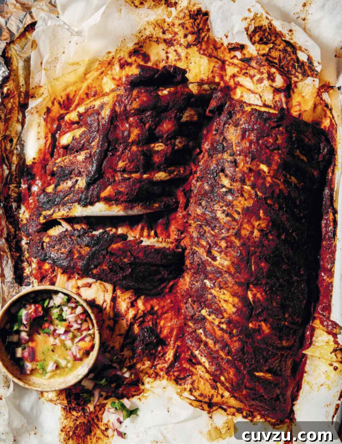 Achiote-Marinated Pibil Pork Ribs 2 Pibil-style pork ribs arranged on parchment paper, accompanied by a vibrant bowl of habanero salsa.