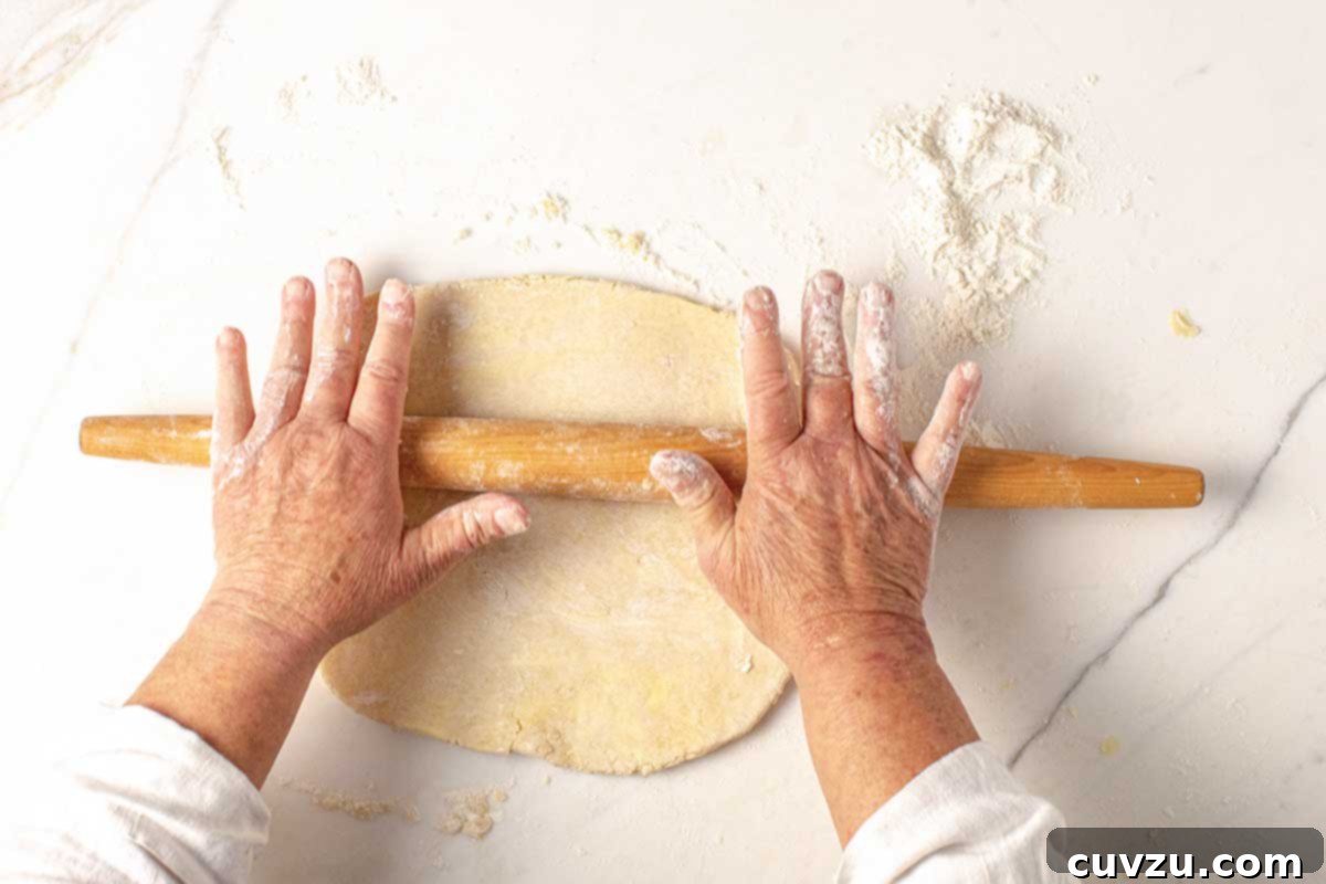 Roll Out a Flawless Pie Crust Every Time 3 A person gently pressing down on a disc of pie dough with a rolling pin, preparing it for a smooth rolling process.