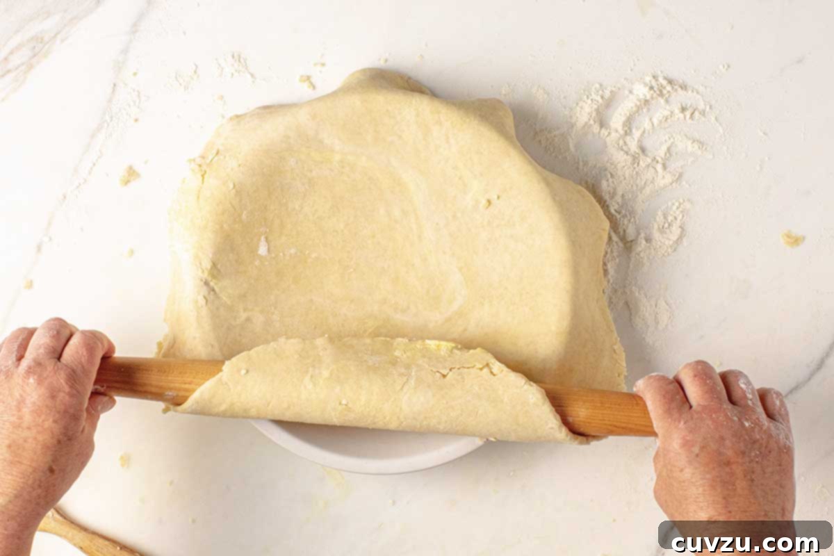Roll Out a Flawless Pie Crust Every Time 7 A person skillfully transferring a rolled out pie crust to a pie plate using a rolling pin, showcasing gentle handling.
