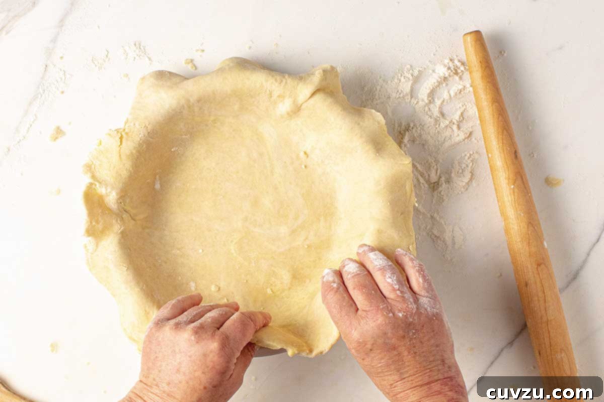 Roll Out a Flawless Pie Crust Every Time 8 A person gently arranging a rolled out pie crust in a pie plate, ensuring it settles without stretching.