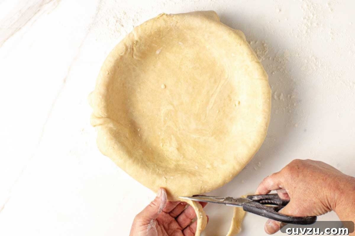 Roll Out a Flawless Pie Crust Every Time 9 A person precisely trimming the edges of a pie crust with scissors, preparing for the final crimping or fluting.