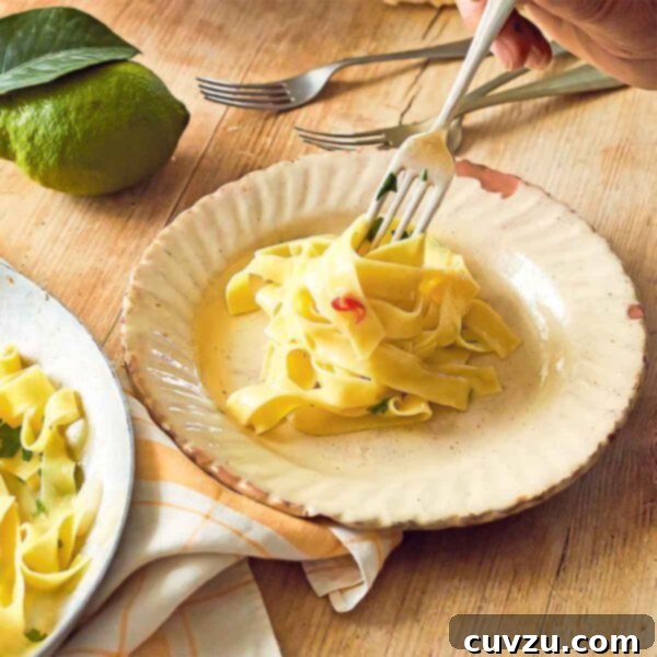 Tagliatelle with lemon on a large serving pate beside a smaller plate with noodles being twirled on a fork. Next to it, there are more forks and some lemons and a chunk of Parmesan.
