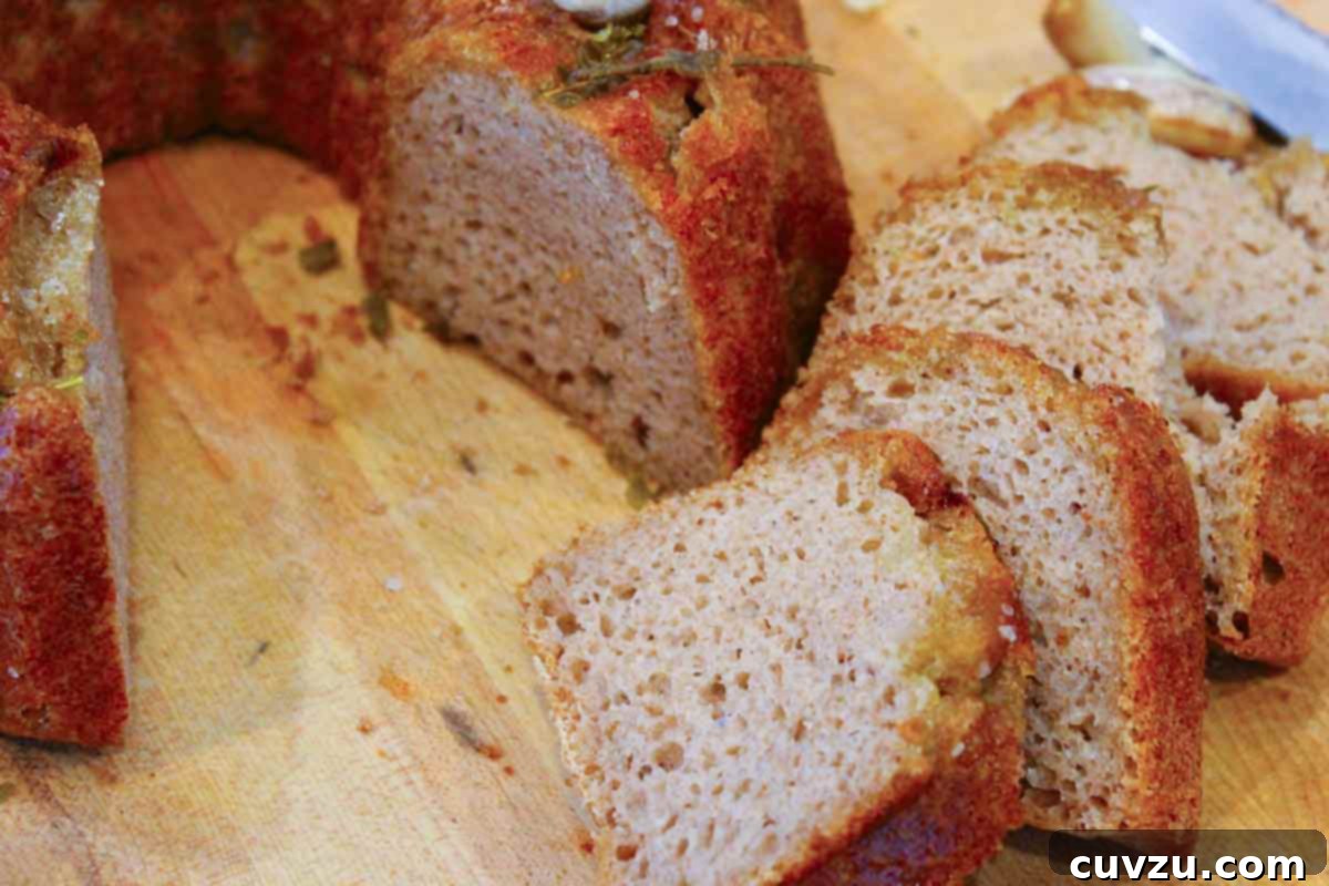 Artisan Rosemary Garlic Sourdough Loaf 9 A close-up shot of Rosemary-Garlic Sourdough Bread made in a Bundt pan, with slices of the bread displayed in the foreground, showing its soft crumb.