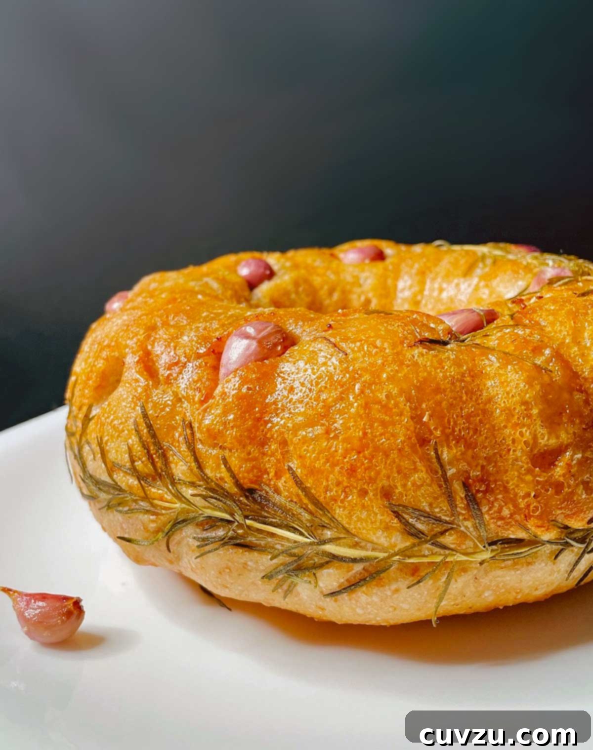 Artisan Rosemary Garlic Sourdough Loaf 3 Rosemary-garlic sourdough bread studded with garlic and rosemary leaves on a plate, highlighting its texture and aromatic inclusions.