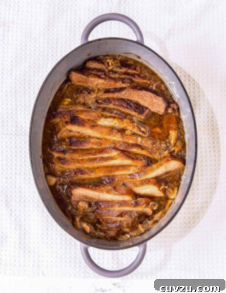 French onion brisket in an oval enamel casserole dish on a white background.