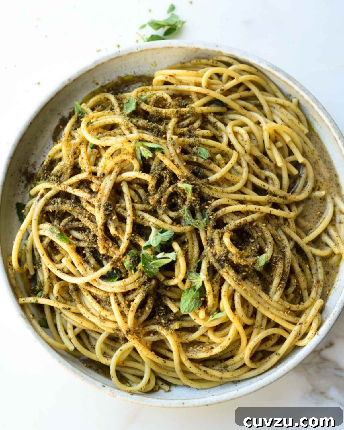 A ceramic bowl filled with za'atar cacio e pepe and topped with fresh marjoram leaves.