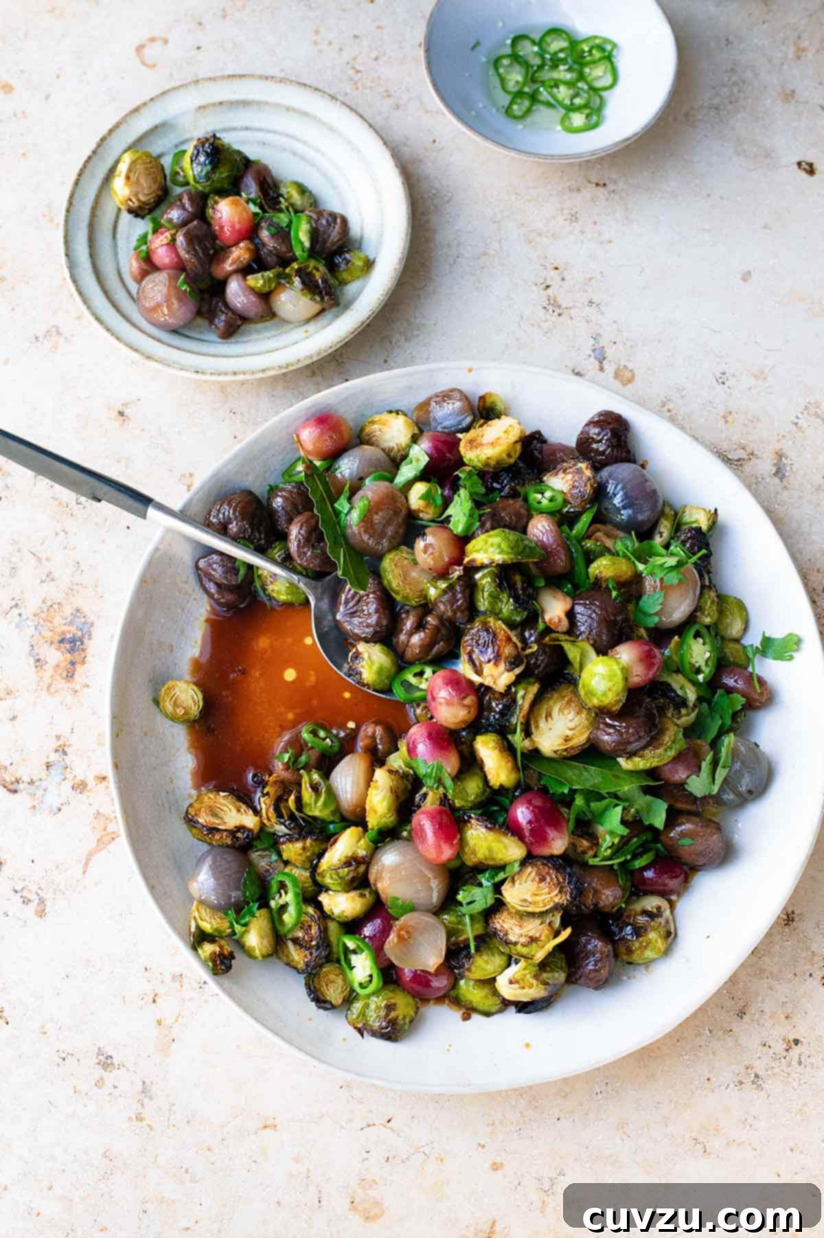 A white bowl filled with sweet and sour brussels sprouts with chestnuts and a serving spoon resting inside.