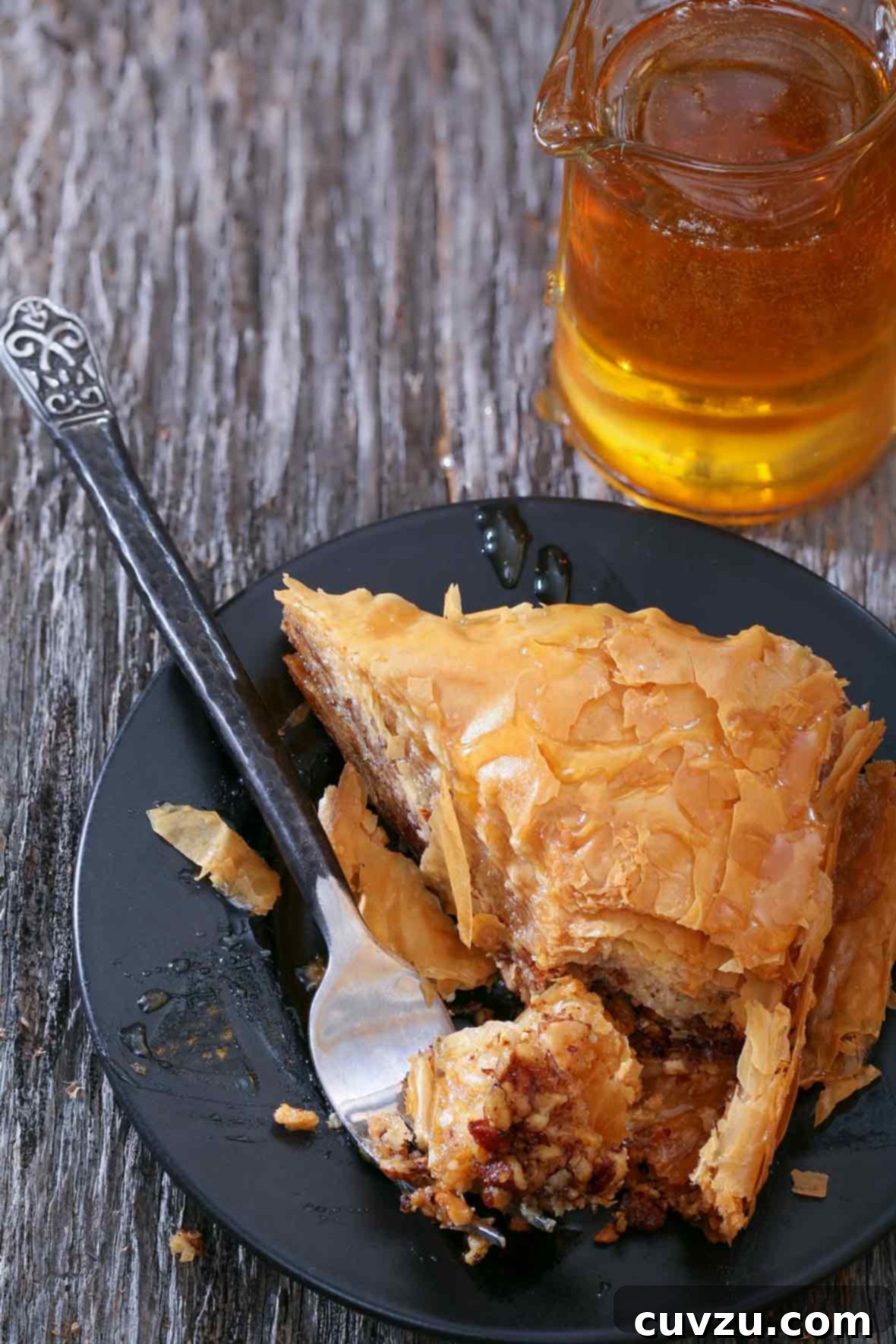 Honey-Drenched Greek Baklava 2 Triangular piece of Greek baklava, with layers of phyllo dough filled with chopped walnuts, drizzled with honey, presented on a black plate. A golden, crispy texture with visible nut layers.