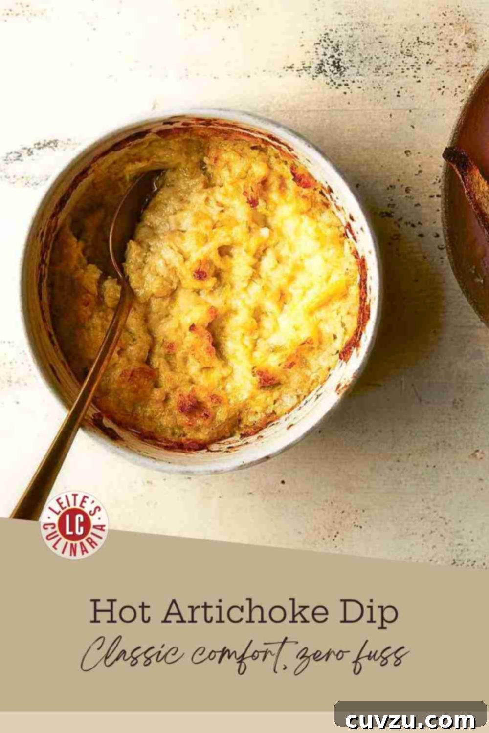 Creamy Baked Artichoke Dip 3 A rustic white bowl overflowing with golden-brown hot artichoke dip, a serving spoon nestled invitingly within its creamy texture.