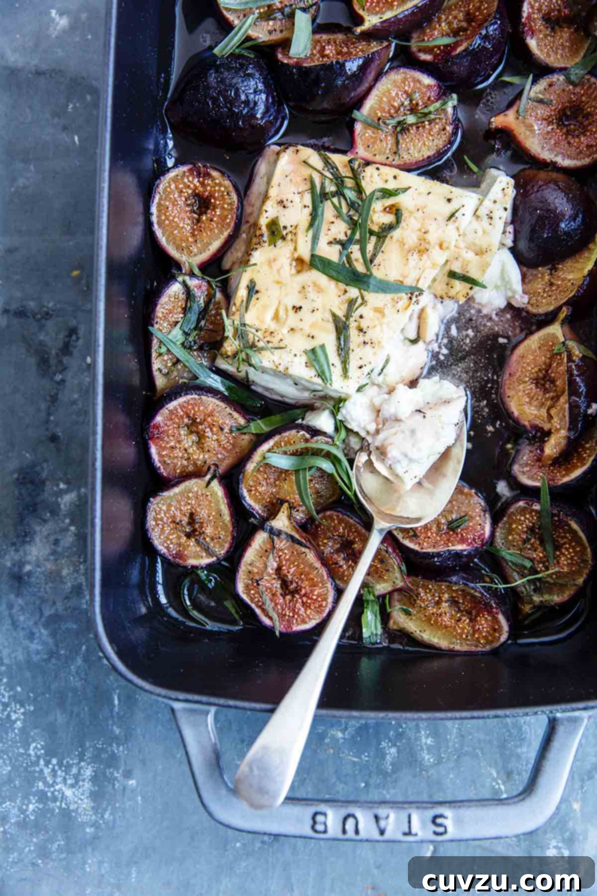 A rectangular baking dish with a block of cooked feta in the center, surrounded by halved figs and tarragon leaves.