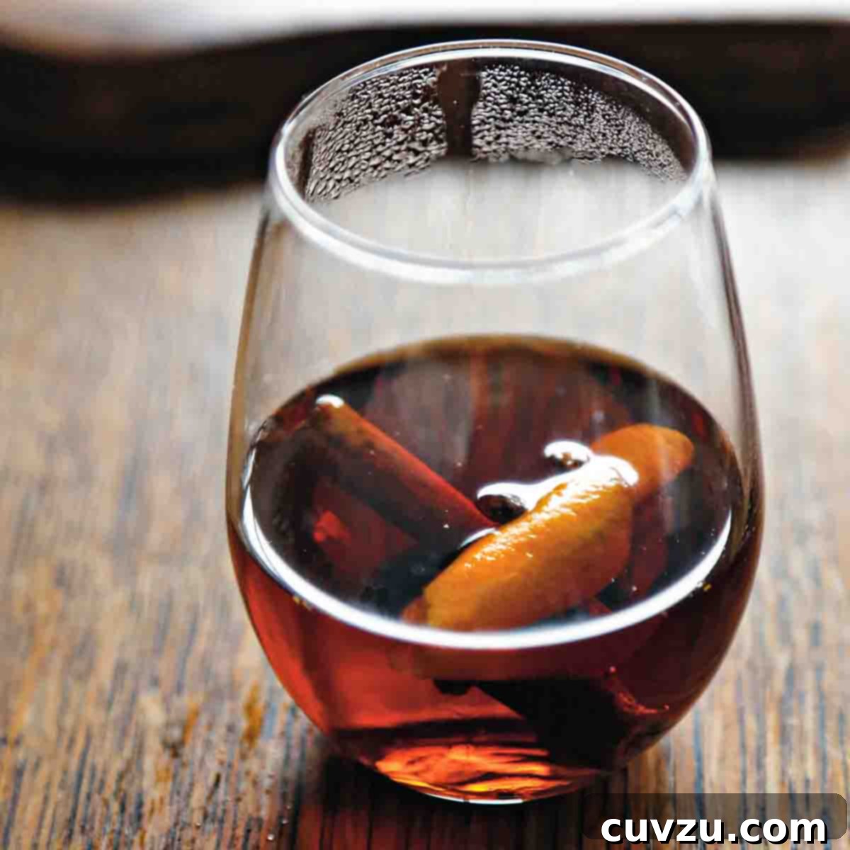 Spiced cider with a cinnamon stick and orange zest, in a stemless wine glass.