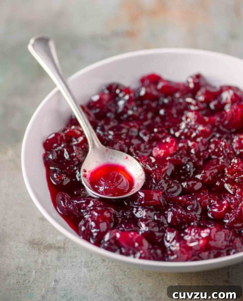 A white bowl filled with whole berry cranberry sauce with a silver spoon resting in it.