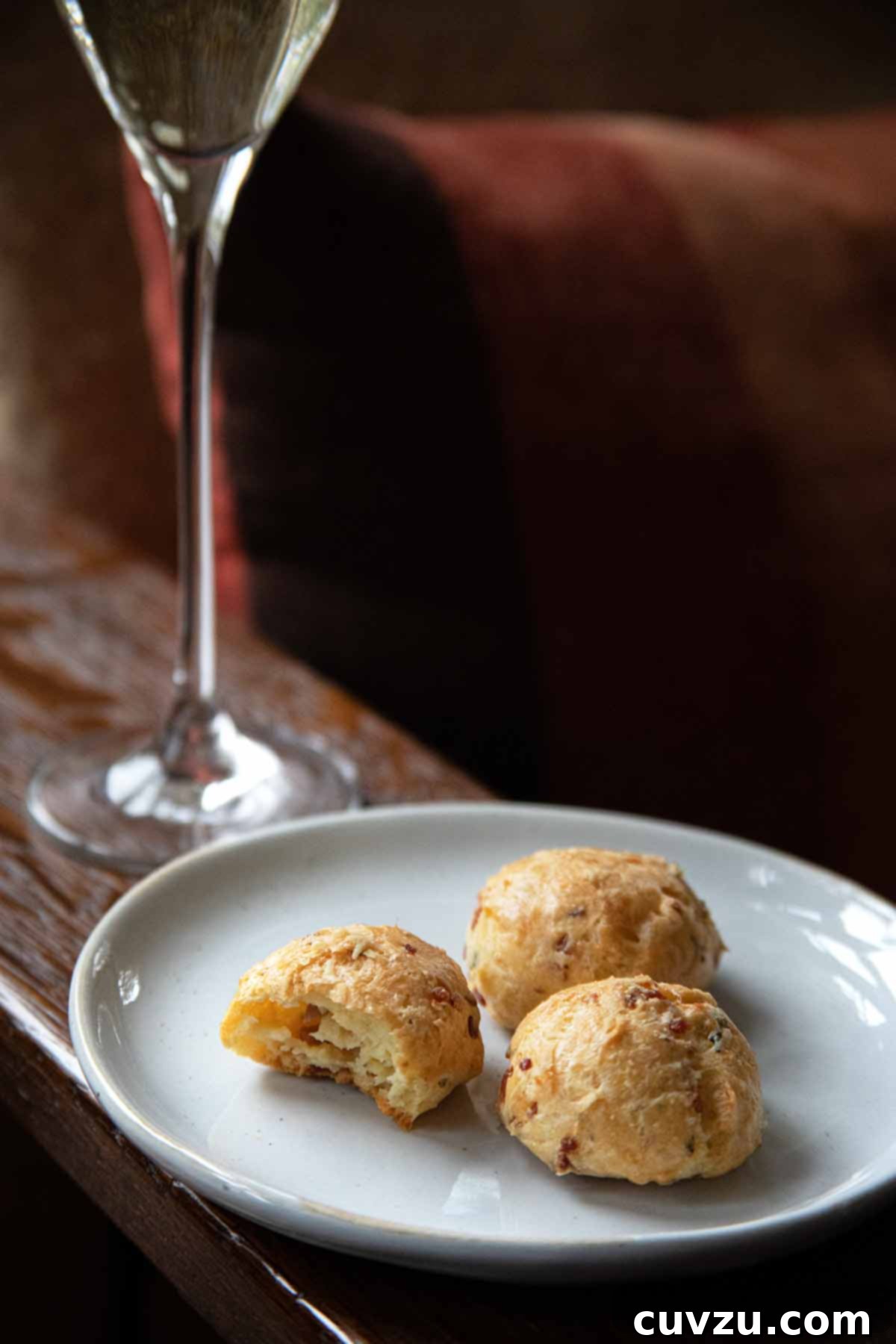 A white plate with three prosciutto-Grana Padano gougeres with a glass of Prosecco in the background.